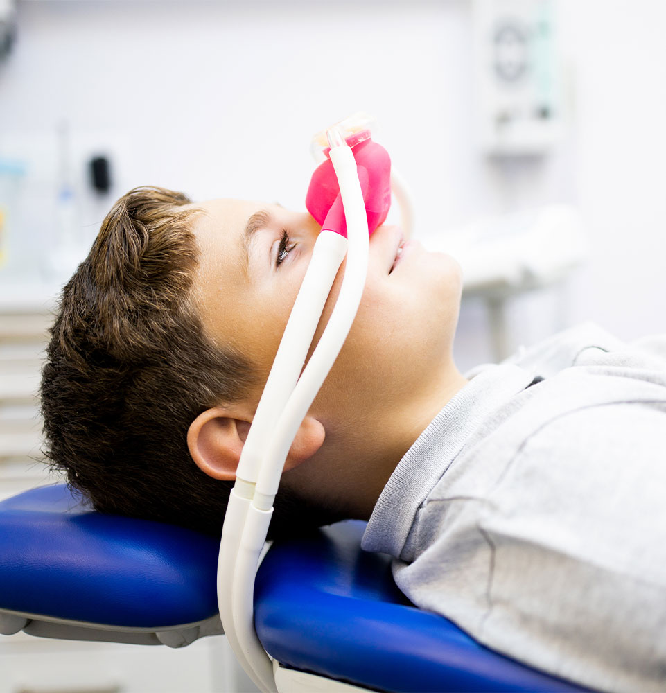 little boy sits in a dentist's office wearing a nasal mask breathing nitrous oxide to relax